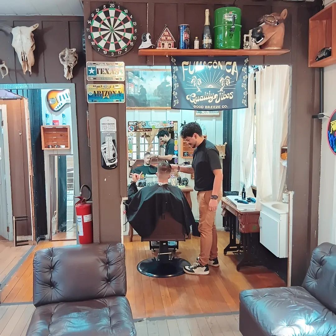 Salão por dentro com sofá de couro e barbeiro atendendo